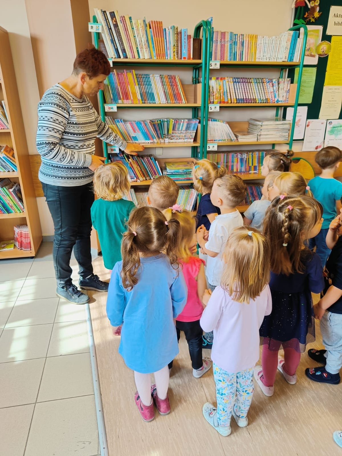 Pani Bibliotekarka pokazuje dzieciom gdzie znajdują się książeczki dla najmłodszych.