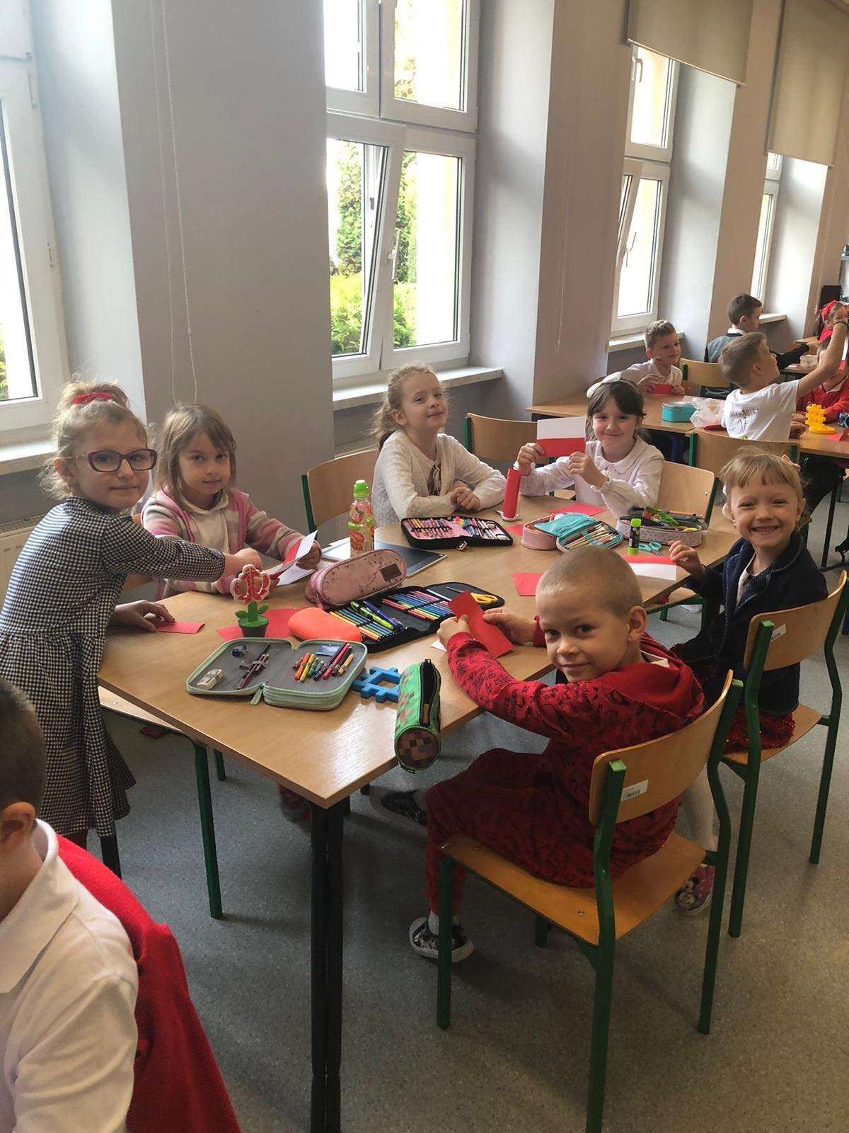 Uczniowie przy stolikach malują flagi Polski