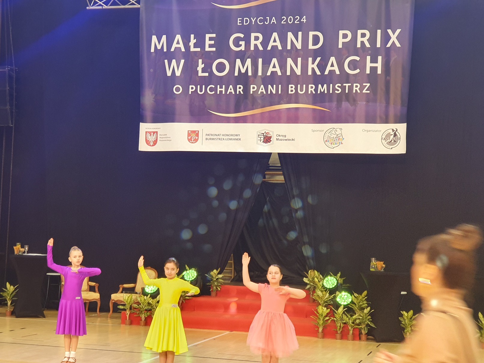 Trzy tancerki w kolorowych sukniach w hali sportowej podczas Ogólnopolskiego Turnieju Tańca Towarzyskiego w Łomiankach