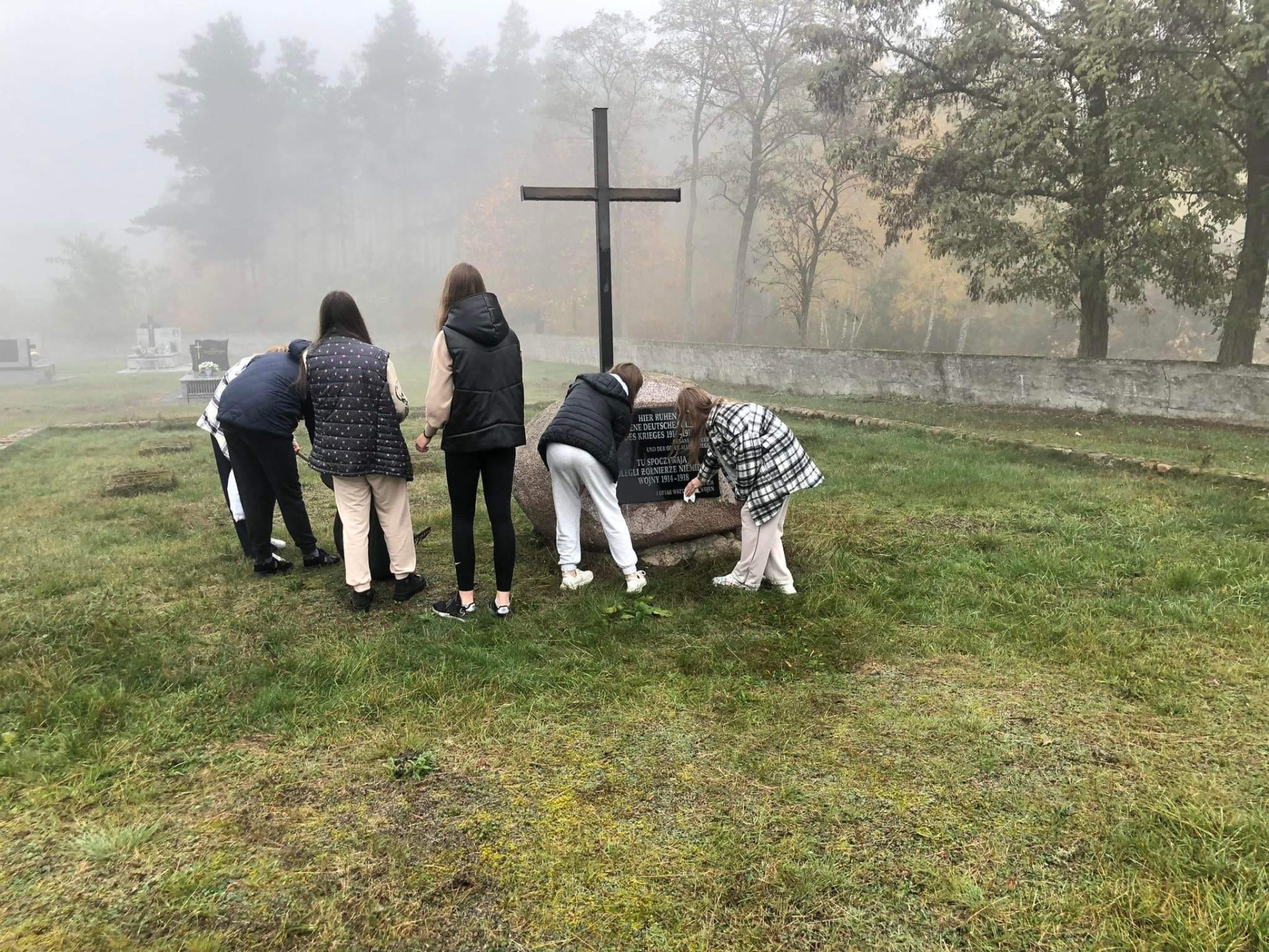 Grupa uczniów w trakcie porządkowania grobu przed dniem Wszystkich Świętych.