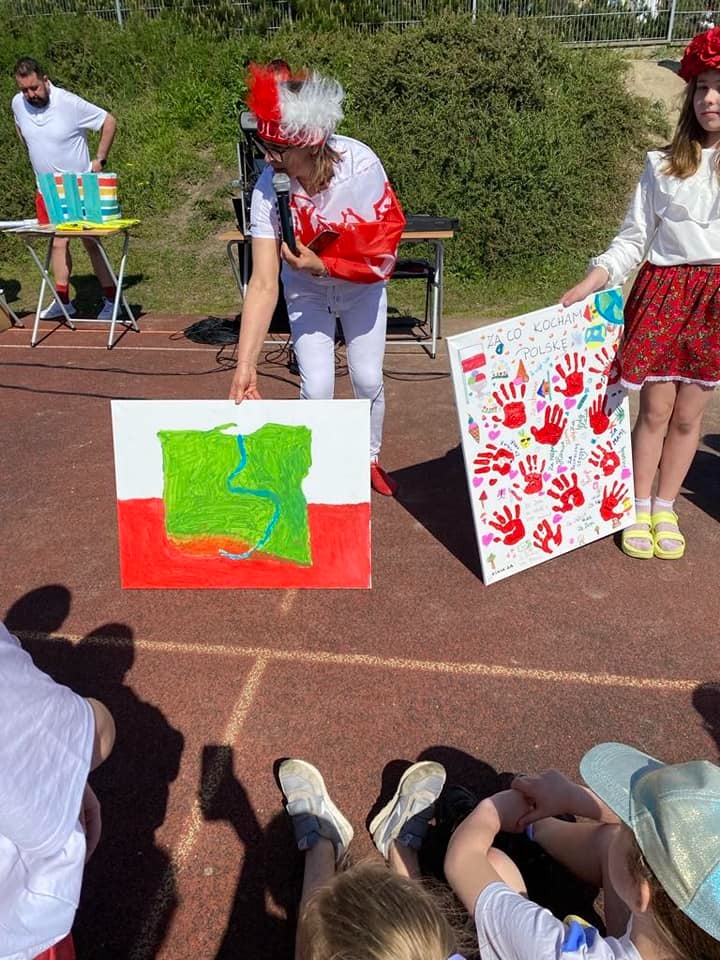Uczniowie w biało-czerwonych strojach demonstrują plakat o Polsce.