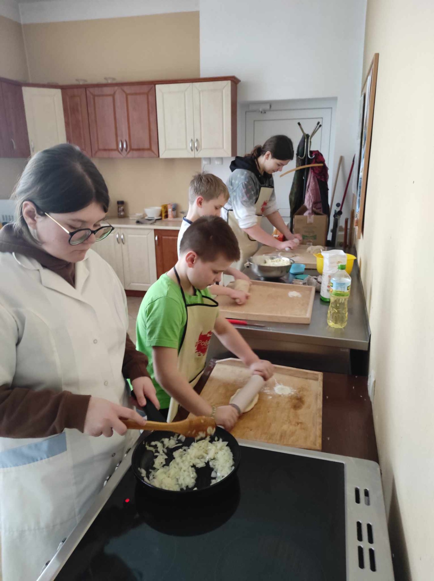 Wychowankowie przygotowują składniki na farsz, dziewczynka smazy cebulę, chłopiec wałkuje ciasto , pozostali mieszają inne składniki