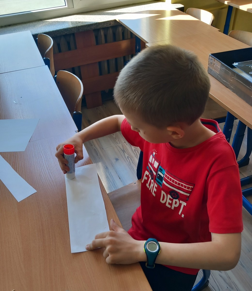 Chłopiec smaruje biały papier klejem