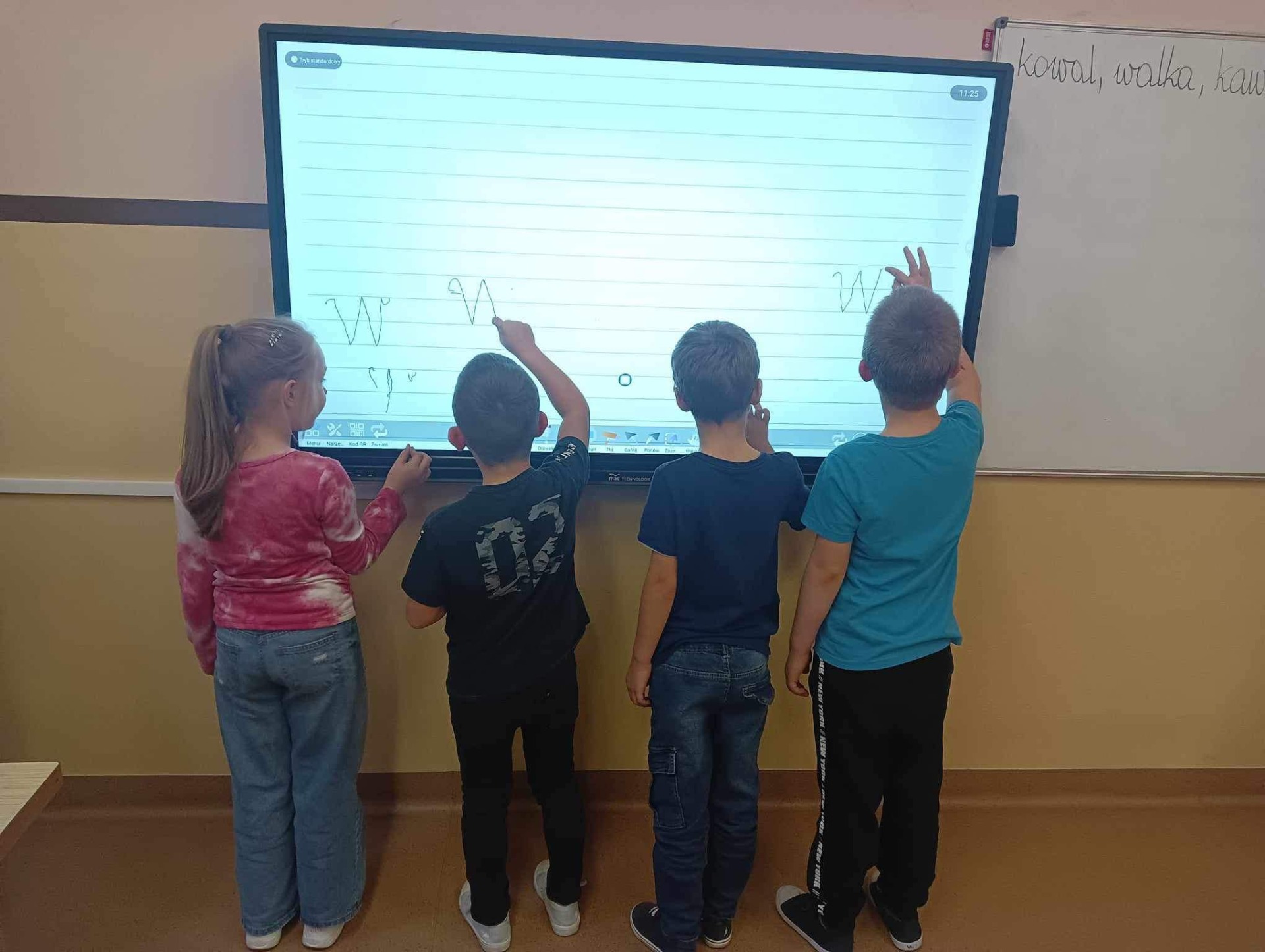 Uczniowie klasy pierwszej piszą literki na nowym monitorze multimedialnym. 