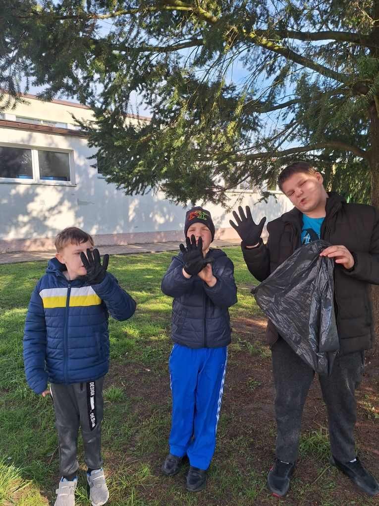 3 uczniów chłopców zbiera śmieci do worka