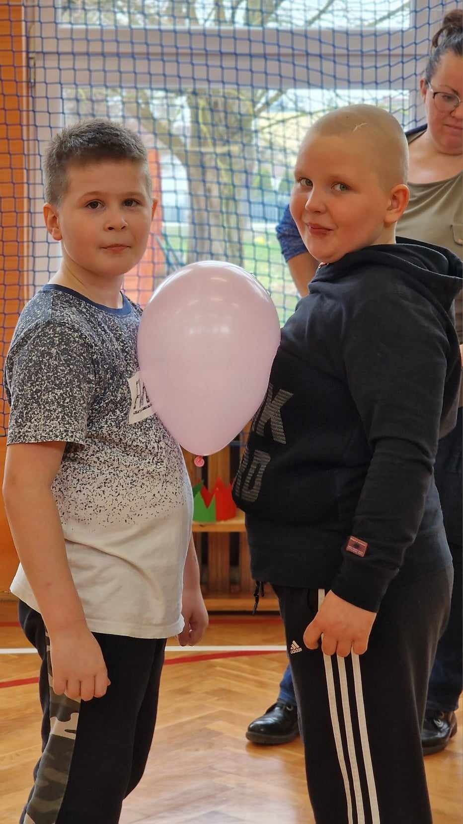 2 chłopców przemieszcza się wzdłuż sali z balonem, który tkwi miedzy ich brzuchami