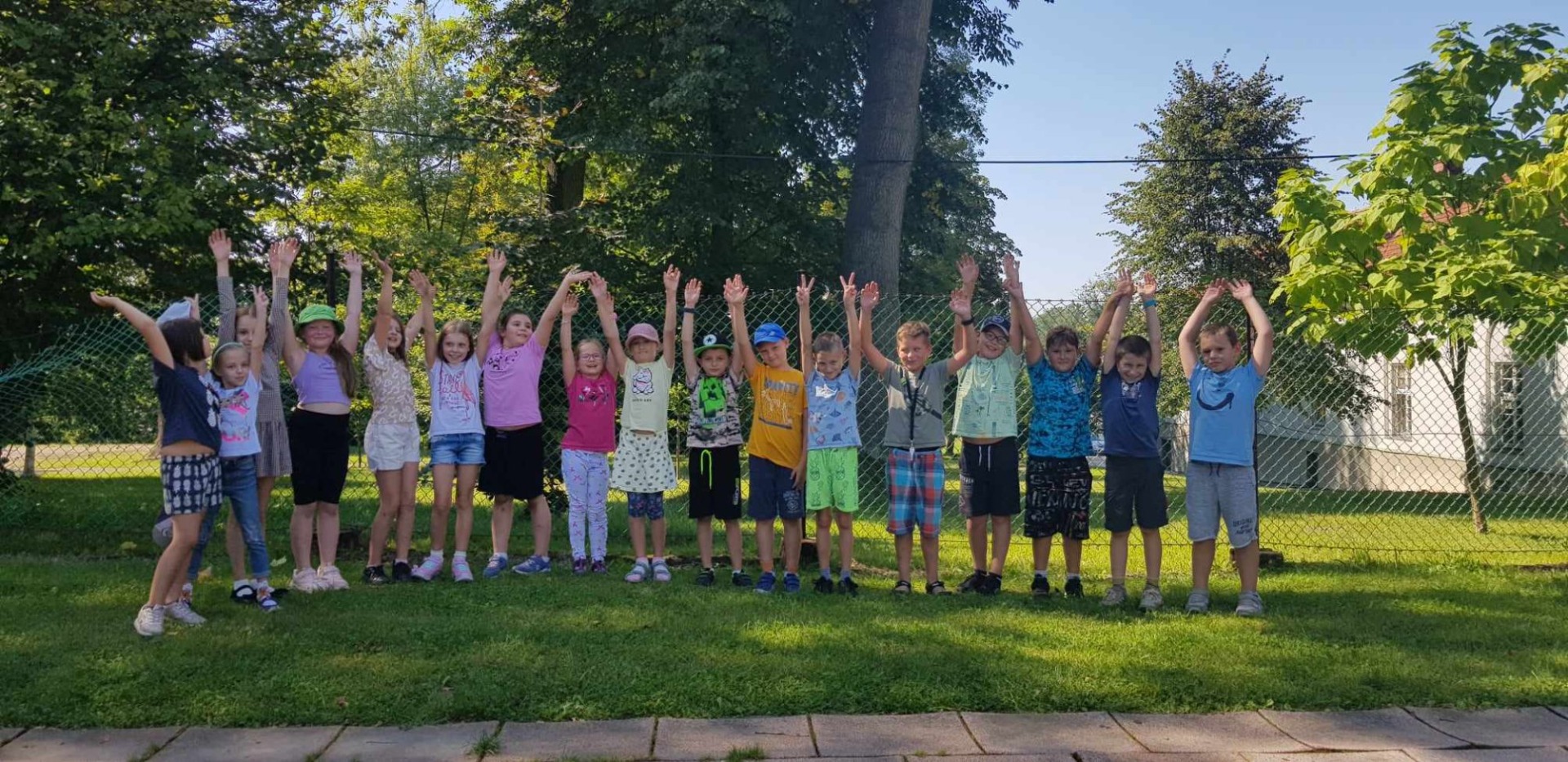 Uczniowie w szkolnym ogrodzie z uniesionymi do góry rękami