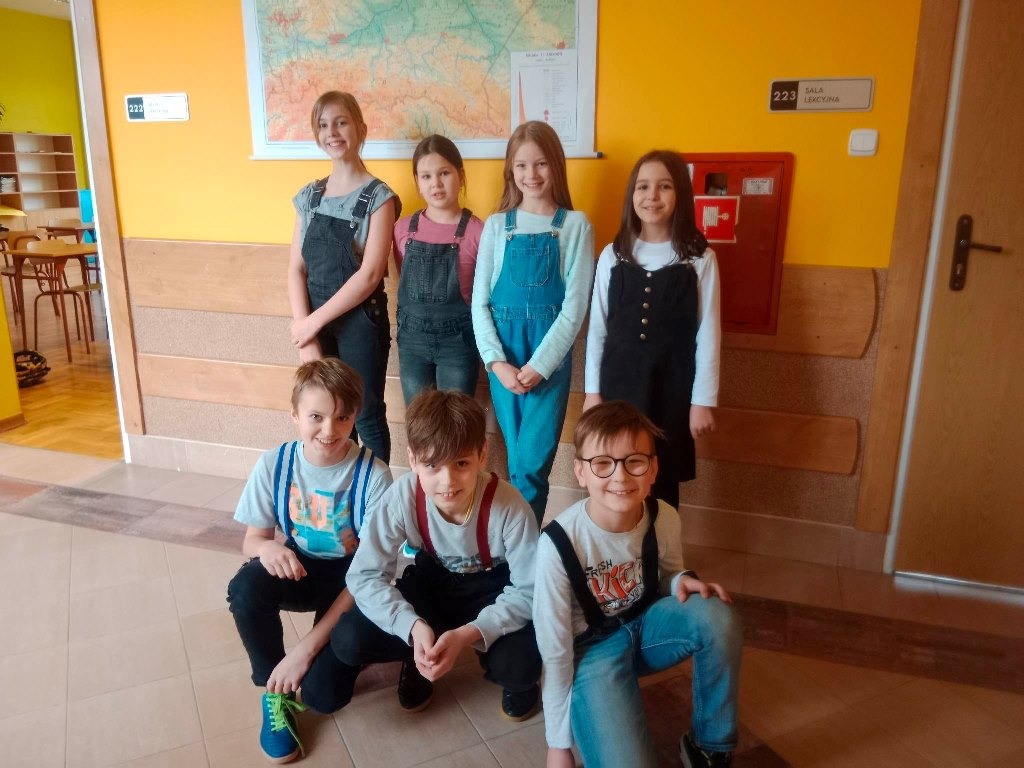 Na piątym zdjęciu na korytarzu szkolnym jest siedmiu uczniów klasy, czwartej trzech chłopców i cztery dziewczynki. Na pierwszym planie klęczą chłopcy, za nimi stoją dziewczynki. Za nimi na ścianie wisi mapa Polski.