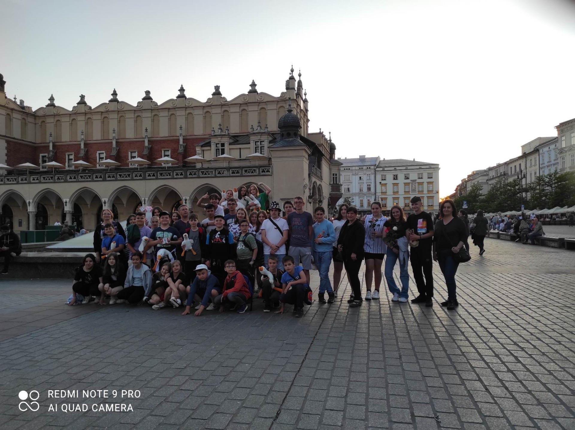 Zdjęcie przedstawia grupę czterdziestu czterech uczniów i nauczycieli stojących na rynku Starego Miasta w Krakowie. Za nimi znajdują się Sukiennice.