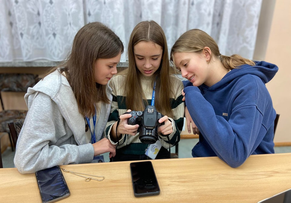 Trzy dziewczynki oglądają aparat fotograficzny.